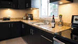 A modern kitchen with dark cabinets, granite countertops, a built-in microwave, a coffee maker, and a wine bottle. - Casa Rama 2. 2 bedroom, 2 bathroom w/ private pool in Cozumel (Cozumel)