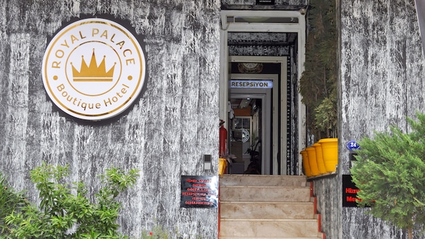 Entrada de un hotel boutique con un cartel que dice 'Royal Palace Boutique Hotel', un área de recepción y una escalera que conduce al interior.