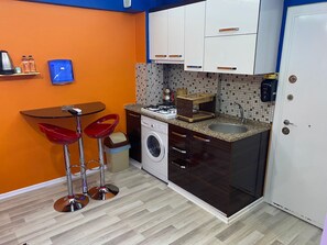Una cocina compacta con lavadora, un lavamanos y un pequeño comedor con dos taburetes.