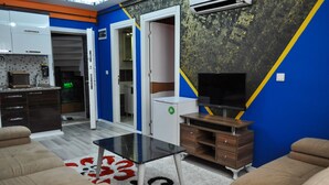 Sala de estar con sofá, una mesa de centro, televisor y una zona de cocina con armarios y microondas.