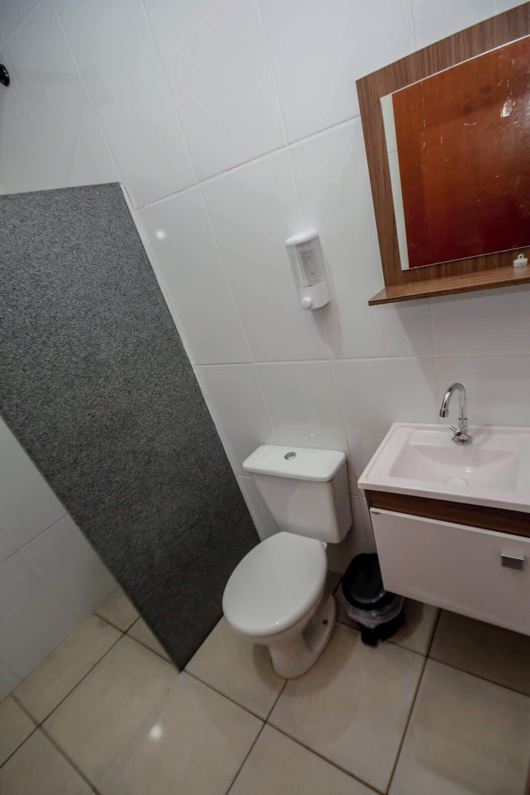 A bathroom with a toilet, sink, and a soap dispenser on the wall.