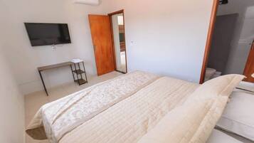 A bedroom with a bed, a TV mounted on the wall, a wooden door, and a small table with a shelf.