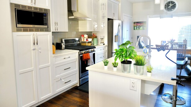 Una cocina moderna con armarios blancos, microondas integrado, refrigerador de acero inoxidable y una pequeña isla con plantas en macetas.