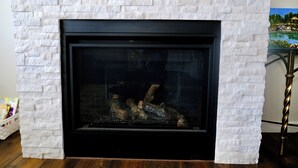 Una chimenea con fachada de ladrillo blanco, marco negro y leña en su interior.