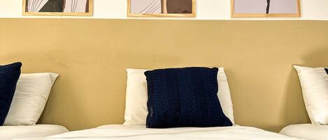 A hotel room with a bed, three framed artworks on the wall, and a plain yellow wall.