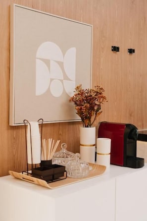 A neatly arranged reception desk with a framed abstract artwork, a vase with dried flowers, a tray with stationery, and a red mail slot.