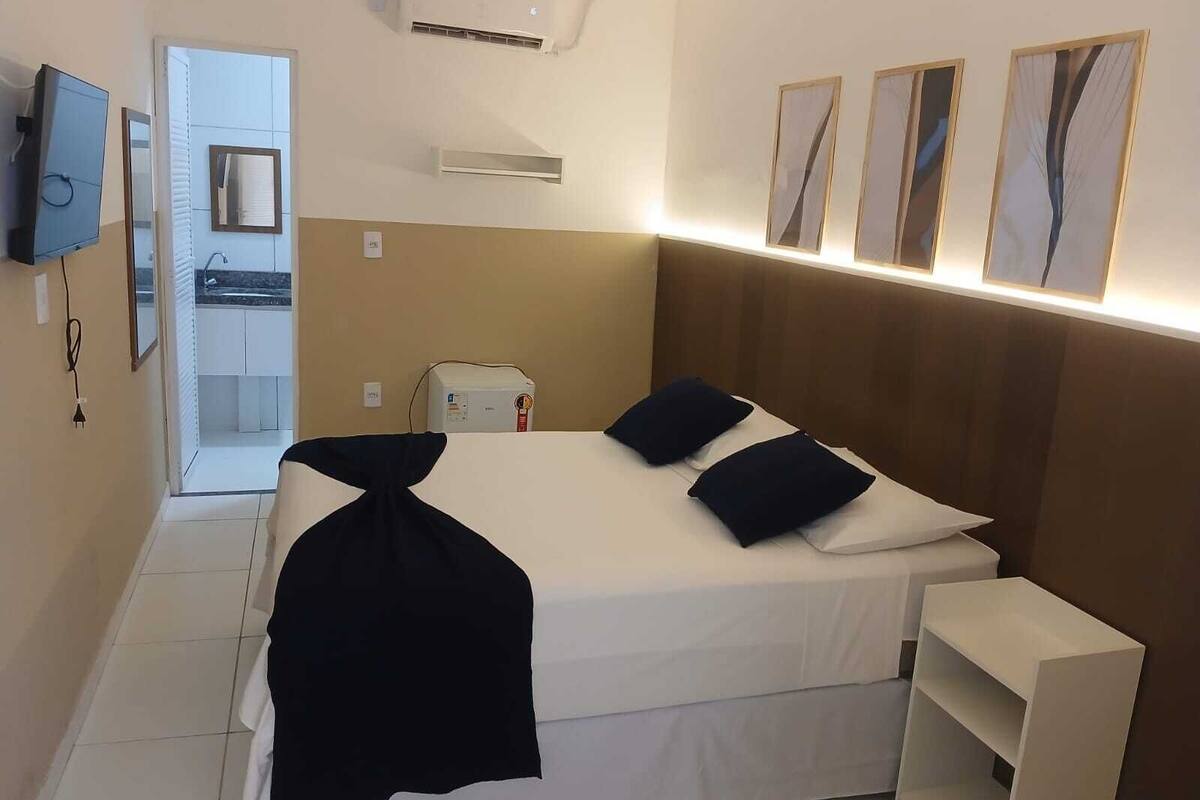 Een hotelkamer met een bed, nachtkastjes, een televisie en een badkamer die door een geopende deur zichtbaar is.