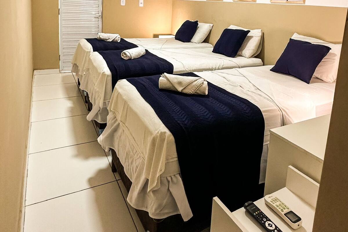Een hotelkamer met drie bedden, een televisie, een nachtkastje met telefoon, en kunst aan de muur.