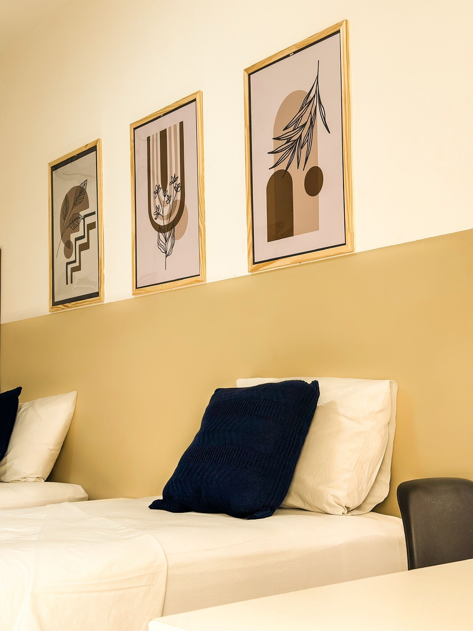Quarto de hotel com uma cama, duas almofadas e três obras de arte emolduradas na parede.