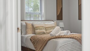 Un lit bien fait, avec un cadre en bois, une literie blanche et un plaid marron.