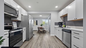 Une cuisine moderne avec des meubles blancs, des appareils en acier inoxydable et une table à manger en bois.