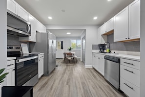 A modern kitchen with white cabinets, stainless steel appliances, and a wooden dining table. - 3BR West End Home w/ Deck & Large Backyard (Atlanta)