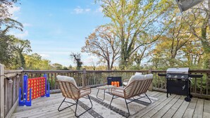 Une terrasse en bois avec deux fauteuils en osier, un barbecue et un jeu de société aux couleurs rouge et jaune.