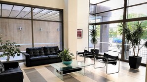 A modern lobby with a glass coffee table, leather sofa, metal chairs, and potted plants.