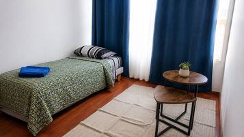 Un dormitorio con cama, una mesa redonda con una planta y una cortina azul.