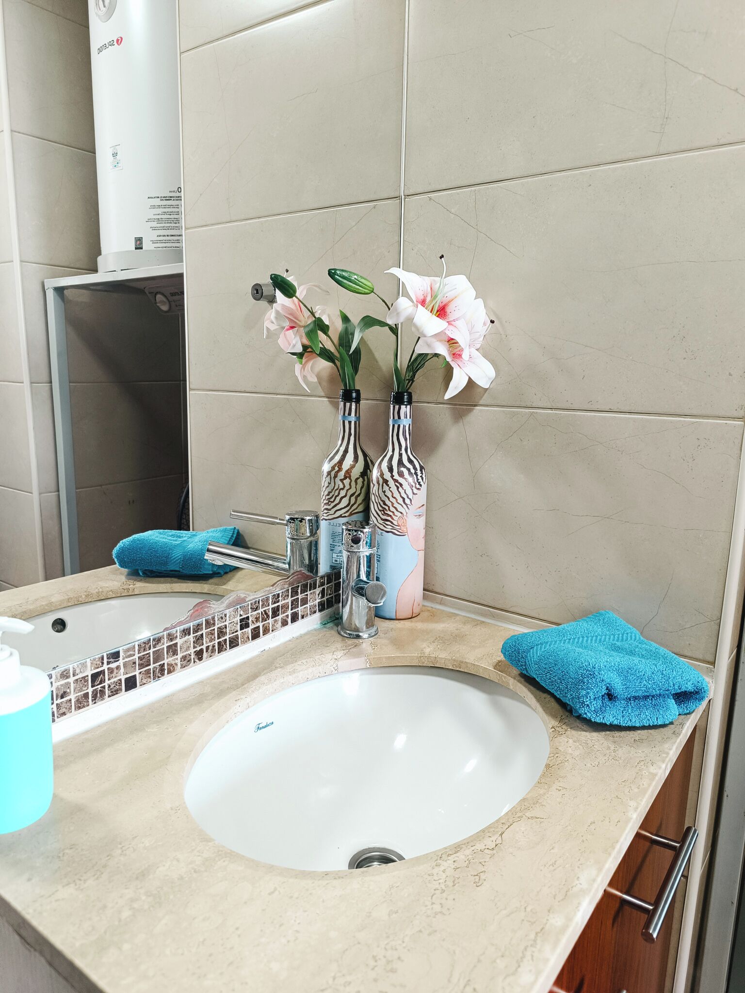 A bathroom with a white sink, two striped vases with flowers, a blue towel, and a mirror.