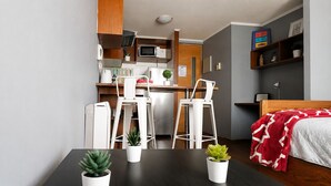 A compact room with a kitchenette, a bed with a red blanket, and two potted plants on the table.