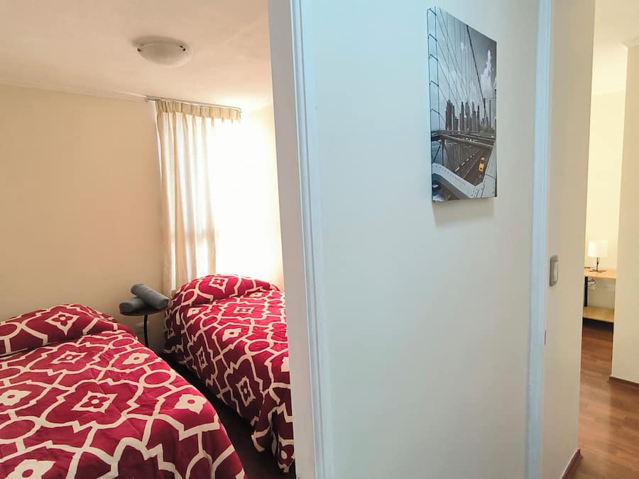 A room with two beds, a window with curtains, a door, and a cityscape painting on the wall.