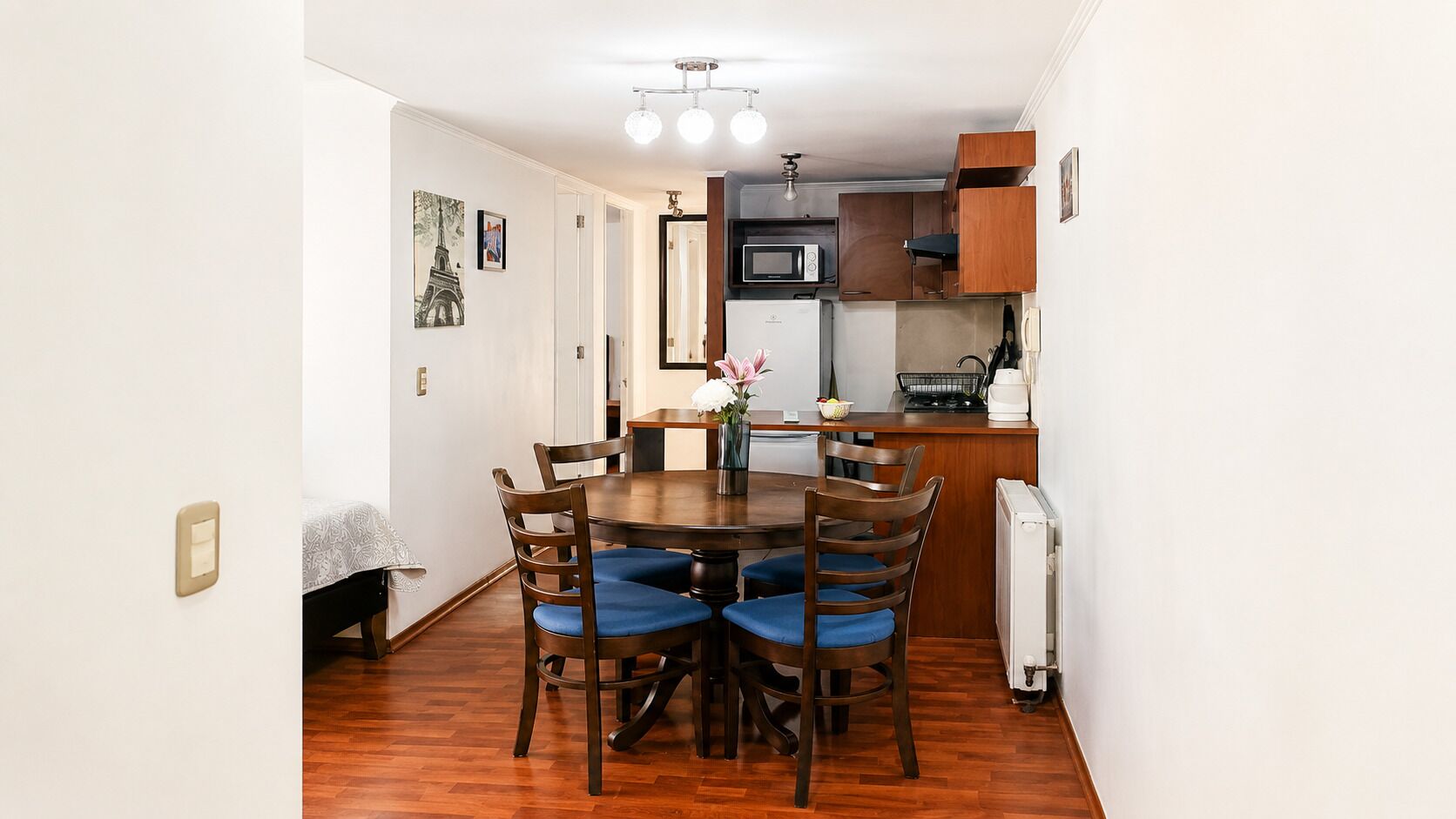 A dining area with a round table, wooden chairs, and a kitchen in the background.