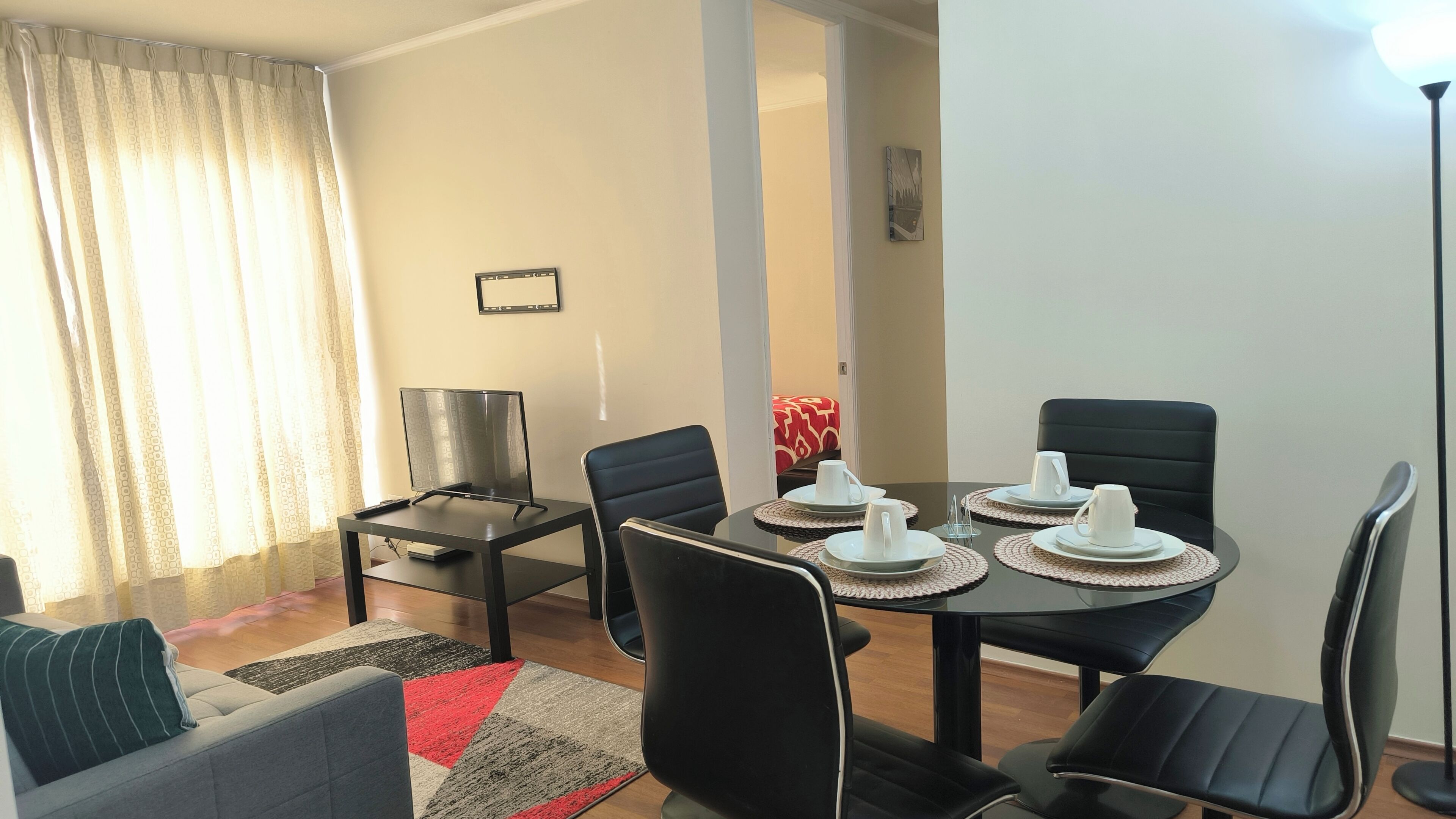 A dining area with a table set for four, a sofa, a TV, and a lamp.