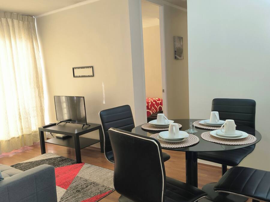 A dining area with a table set for four, a sofa, a TV, and a lamp.