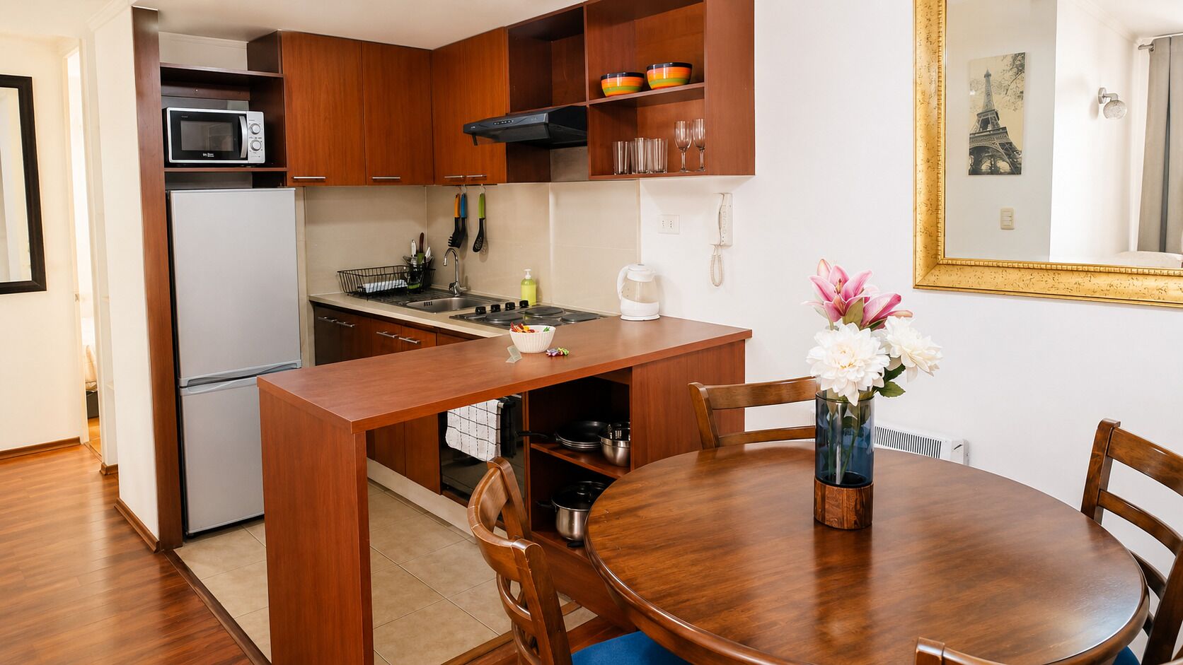 A compact kitchen with wooden cabinets, a built-in microwave, a gas stove, and a dining area with a round wooden table and chairs.