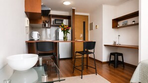 A compact kitchen with a microwave, refrigerator, and a dining area with two chairs and a small stool.