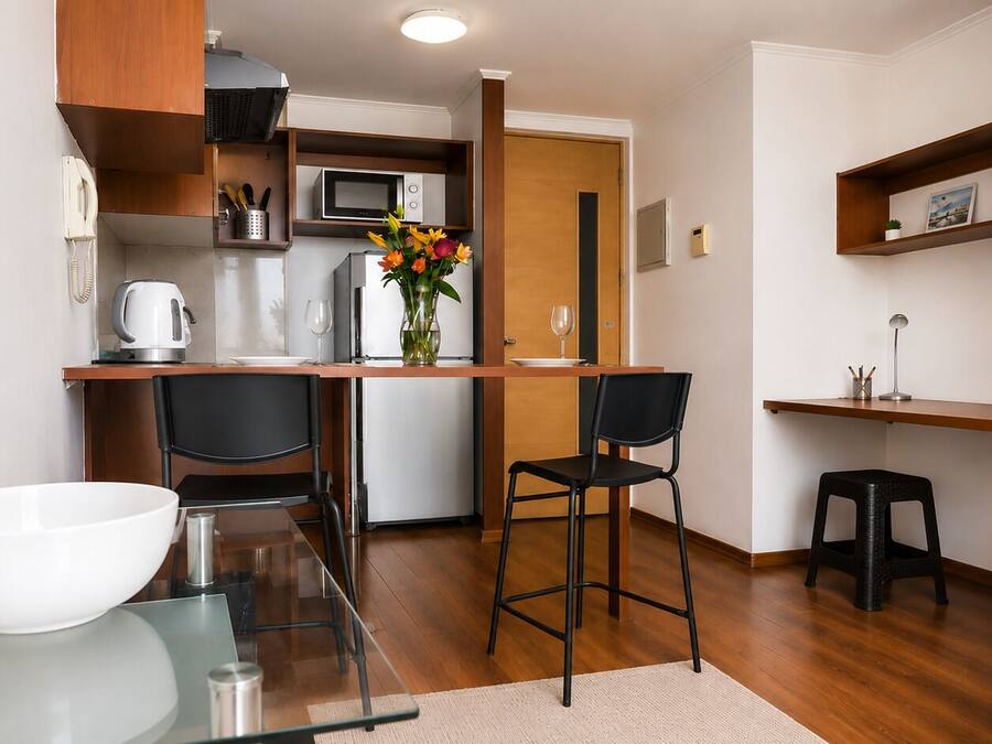 A compact kitchen with a microwave, refrigerator, and a dining area with two chairs and a small stool.