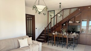 A living room with a sofa, a dining table set for four, a staircase, and wooden cabinets. - ClickSardegna Villa Garden in Alghero for 10 Guests with Garden (Alghero)
