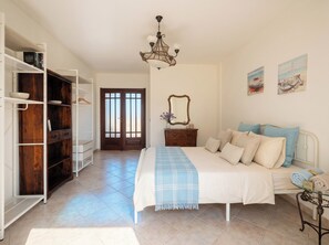 Ein Schlafzimmer mit Bett, Kommode, Kleiderschrank, einer Chandelierleuchtre und Kunstwerken an den Wänden.