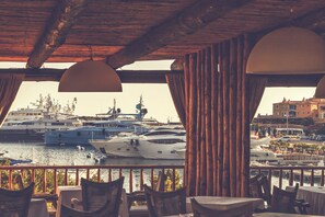 Ein Restaurant mit Blick auf eine Marina, Holzmöbel und hängende Lampen.