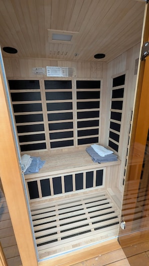 A sauna room with wooden slats, a bench, and a vent at the bottom.