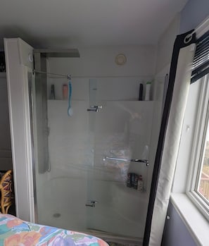 A glass-enclosed shower with a handle, a towel rack, and a small shelf with toiletries.