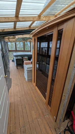 A wooden deck with a glass enclosure, a small table, and a bench.