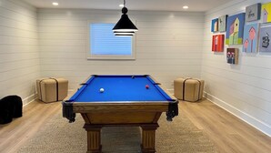 A pool table in a room with white paneled walls, a window with blinds, and artwork on the wall. - LAKEFRONT PROPERTY l DANCING BEAR (Lake Toxaway)