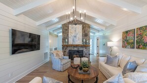 A spacious living room with a stone fireplace, a large flat-screen TV, and a cozy seating area with a coffee table. - LAKEFRONT PROPERTY l DANCING BEAR (Lake Toxaway)