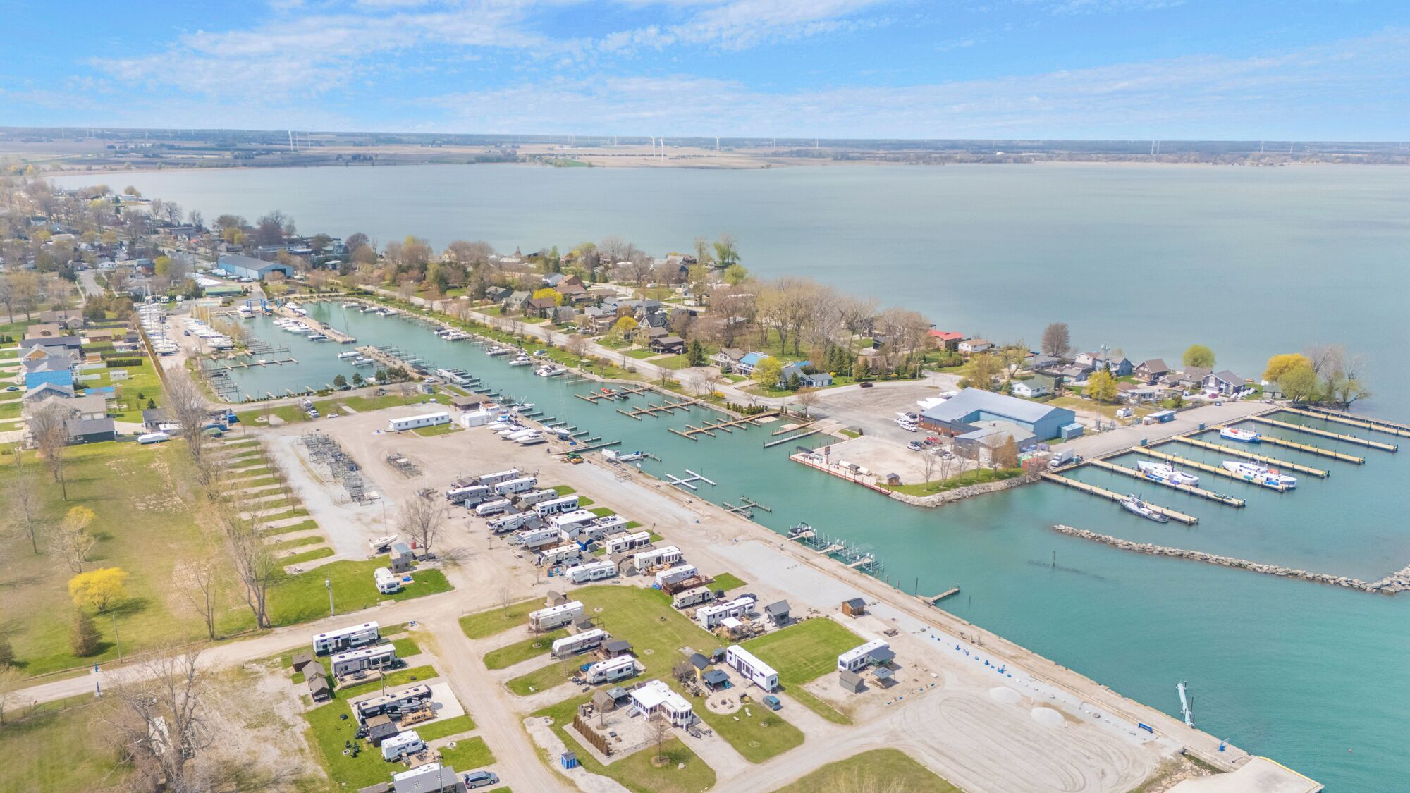 Luchtbeeld van een jachthaven met aan wal liggende boten, een parkeerplaats met campers en een woongebied met huizen en bomen.