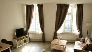 Een woonkamer met een televisie, bank, salontafel en ramen met gordijnen.