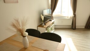 Een kamer met een houten tafel, een vaas met veren, een klok, een televisie en een radiator.