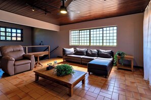 Una sala de estar moderna con sofá, sillón y mesa de centro, suelo de madera y ventanas amplias.