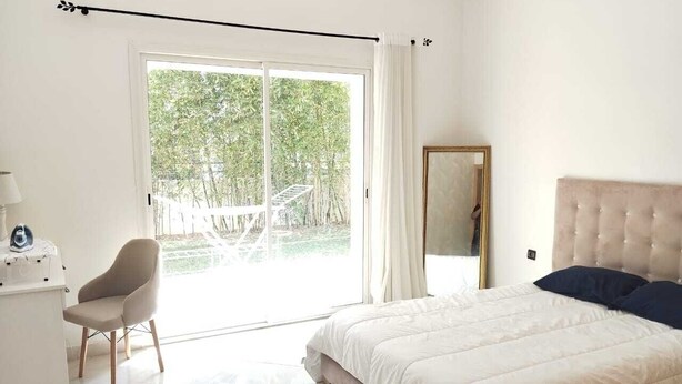 Une chambre avec un lit, une chaise, un miroir et une vue sur la verdure, visible à travers une porte coulissante.