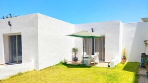 Un bâtiment moderne de couleur blanche, doté d’un patio, d’une table avec des chaises et de plantes en pot.