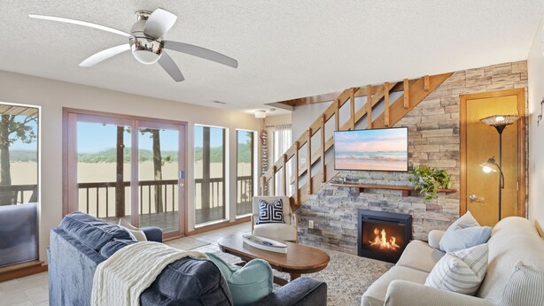 Una sala de estar con chimenea, ventilador de techo, escalera y un amplio ventanal con vistas panorámicas.