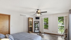 Un dormitorio con una cama, ventilador de techo, ventana y puerta.