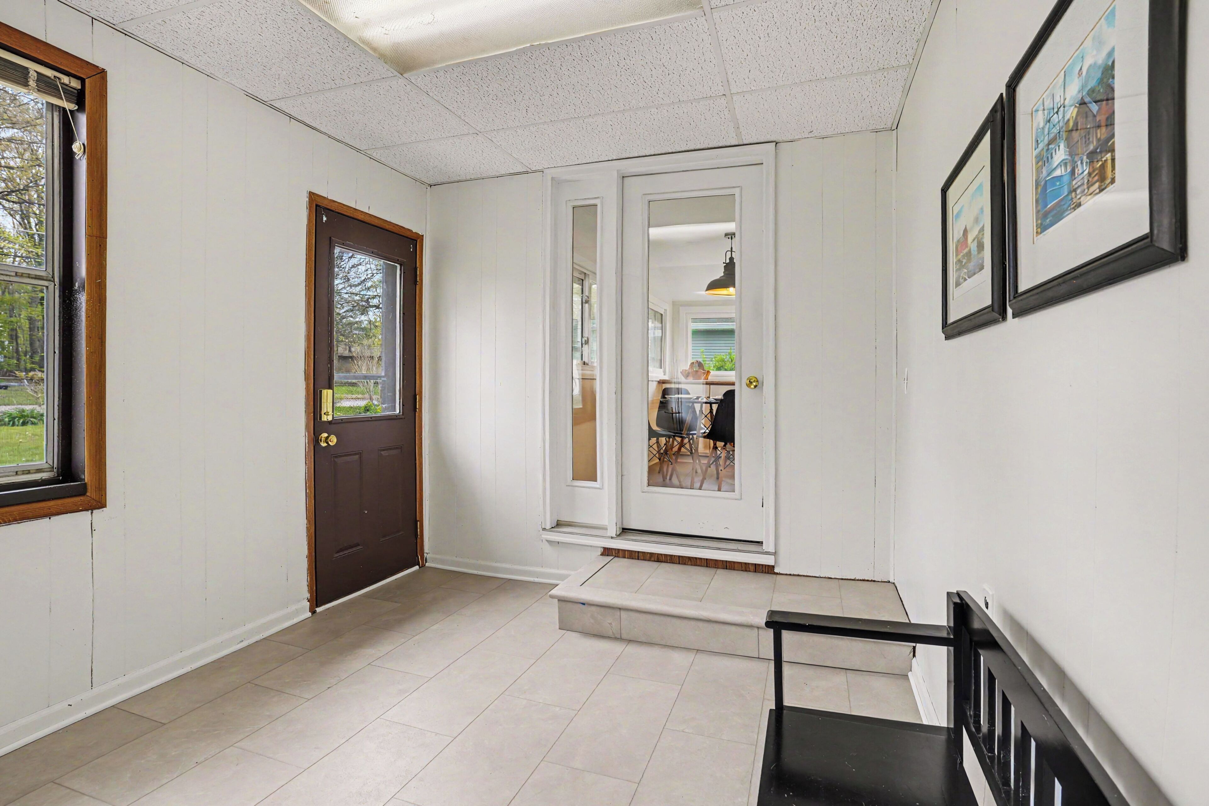 A hallway with a door, a staircase, and a dining area visible through an open door.
