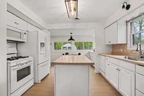 A modern kitchen with white cabinetry, a central island, a stove, and a large window providing a view of the outdoors.