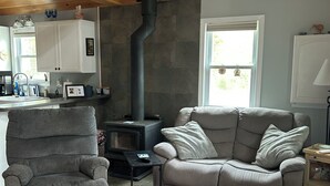 Ein gemütliches Wohnzimmer mit Kamin, einem grauen Sessel, einer Couch und einem kleinen Tisch.