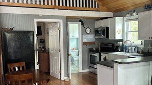Eine Küche mit Holzboden, einem Essbereich mit Tisch und Stühlen, einem Kühlschrank und einem Deckenventilator.