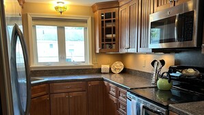 A kitchen with wooden cabinets, stainless steel appliances, a window, and recessed ceiling lights. - Pines Cottage – Yarmouth w/ Private Beach Rights (Yarmouth)