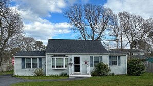 A single-story house with a front porch, a mailbox, and a small front yard. - Pines Cottage – Yarmouth w/ Private Beach Rights (Yarmouth)